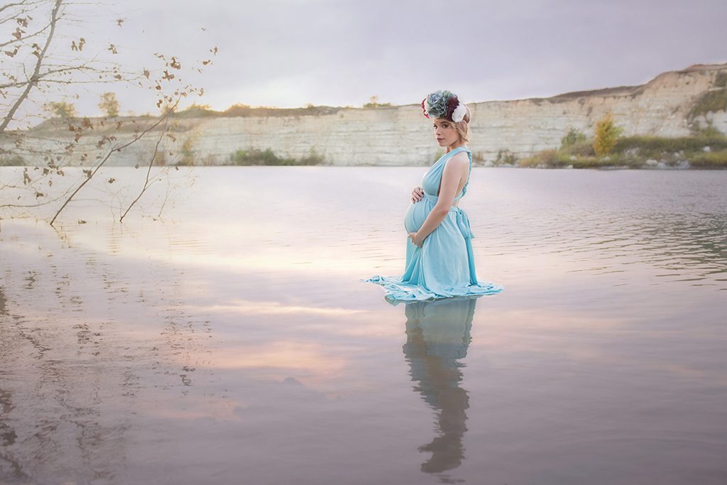 Dallas mom to be wading in the lake at sunset wearing a blue dress and floral corwn