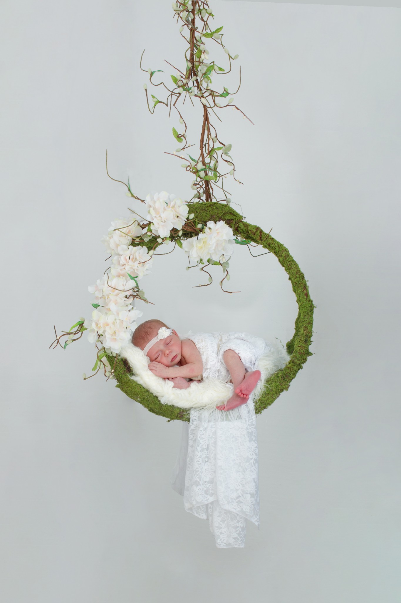 Composite newborn image of baby in floral and moss swing on a white background.