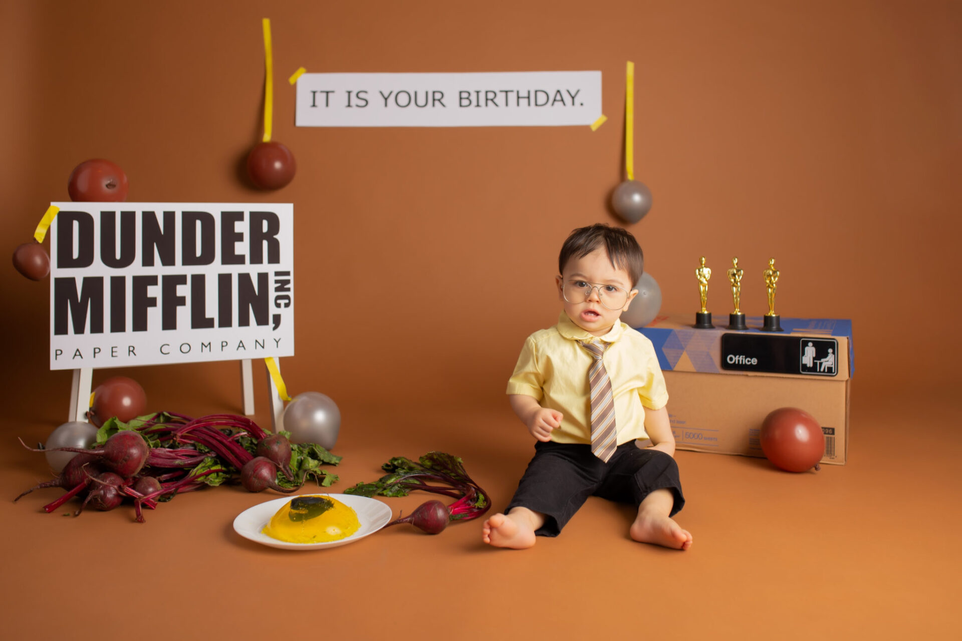 Dallas cake smash photographer designed Office themed one year birthday photography session with a baby Dwight Schrute complete with a stapler in jello, It is your birthday sign and dundees in the background.