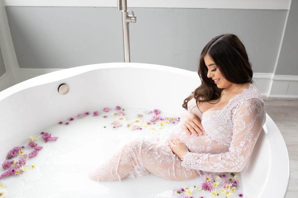pregnant mom pictured during maternity photo shoot milk bath session at origins birth services dallas on swiss avenue. Mother is pictured in bath of milk and flowers in birthing suite in birth center run by midwife Amy Tate