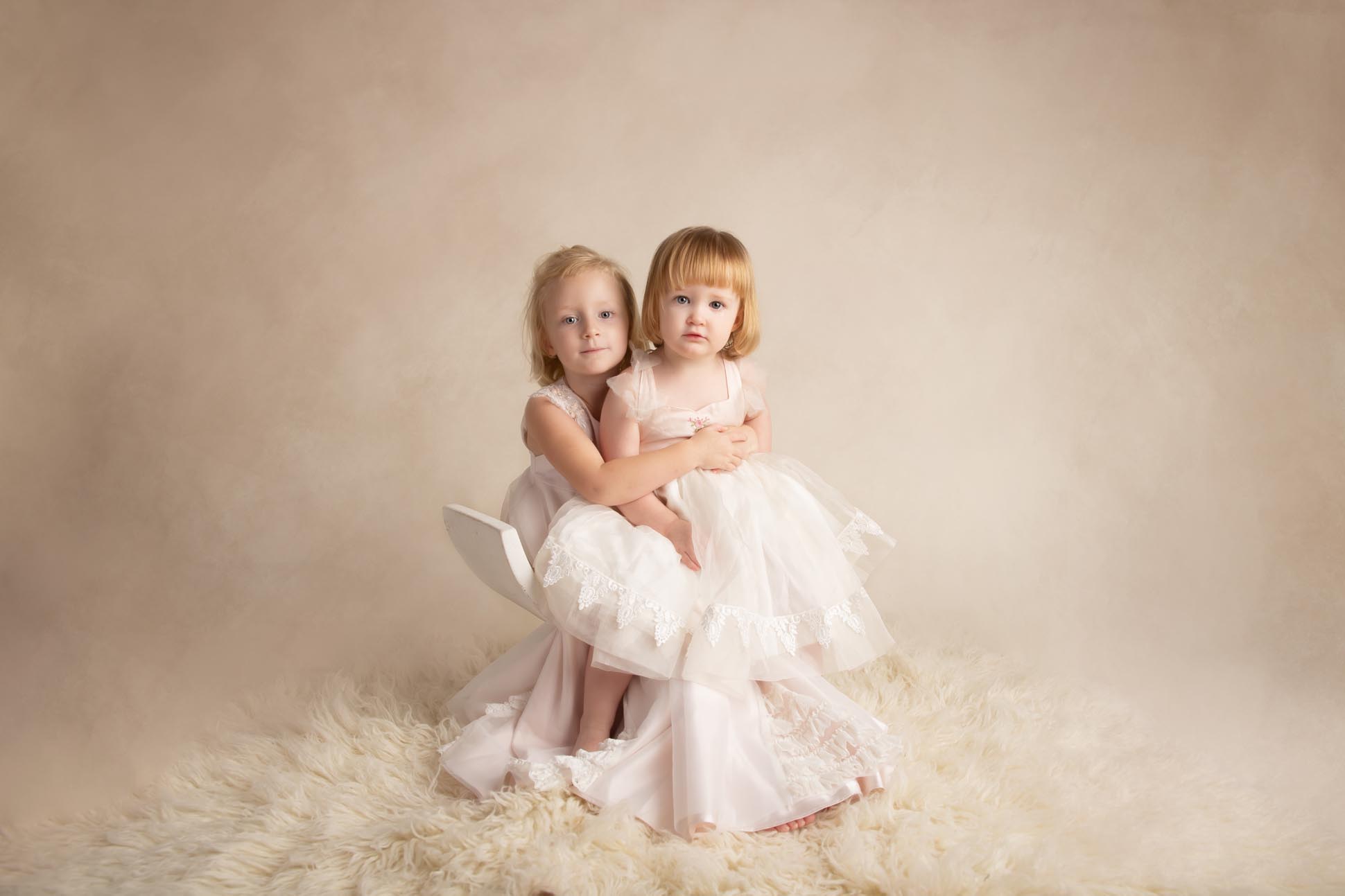 Dallas child photographer shares picture of two young sisters on cream background both wearing cream colored dresses