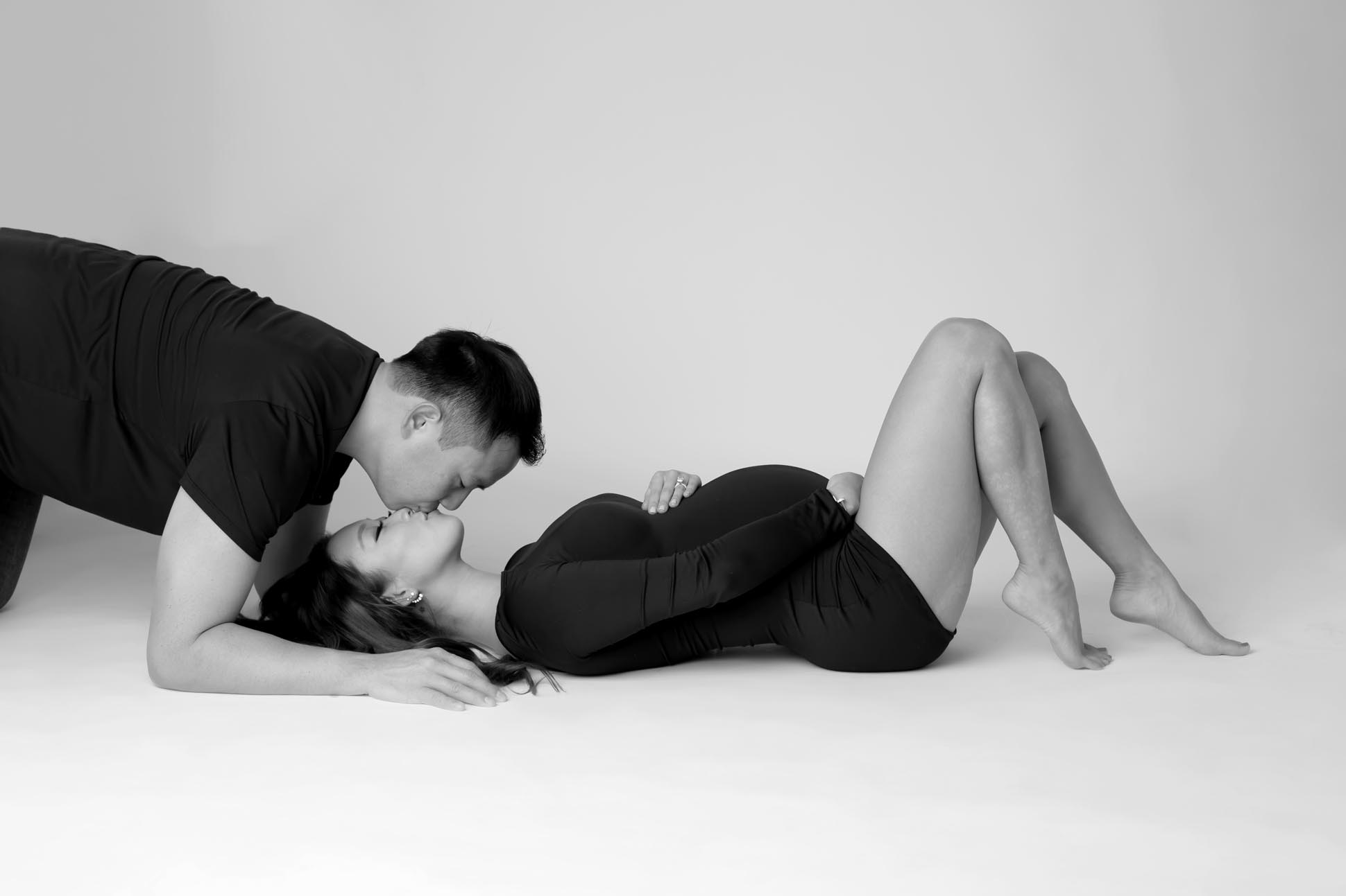 Dallas maternity photographer poses couple with mom to be lying on her back on the floor and new dad hovering giving her an upside down kiss