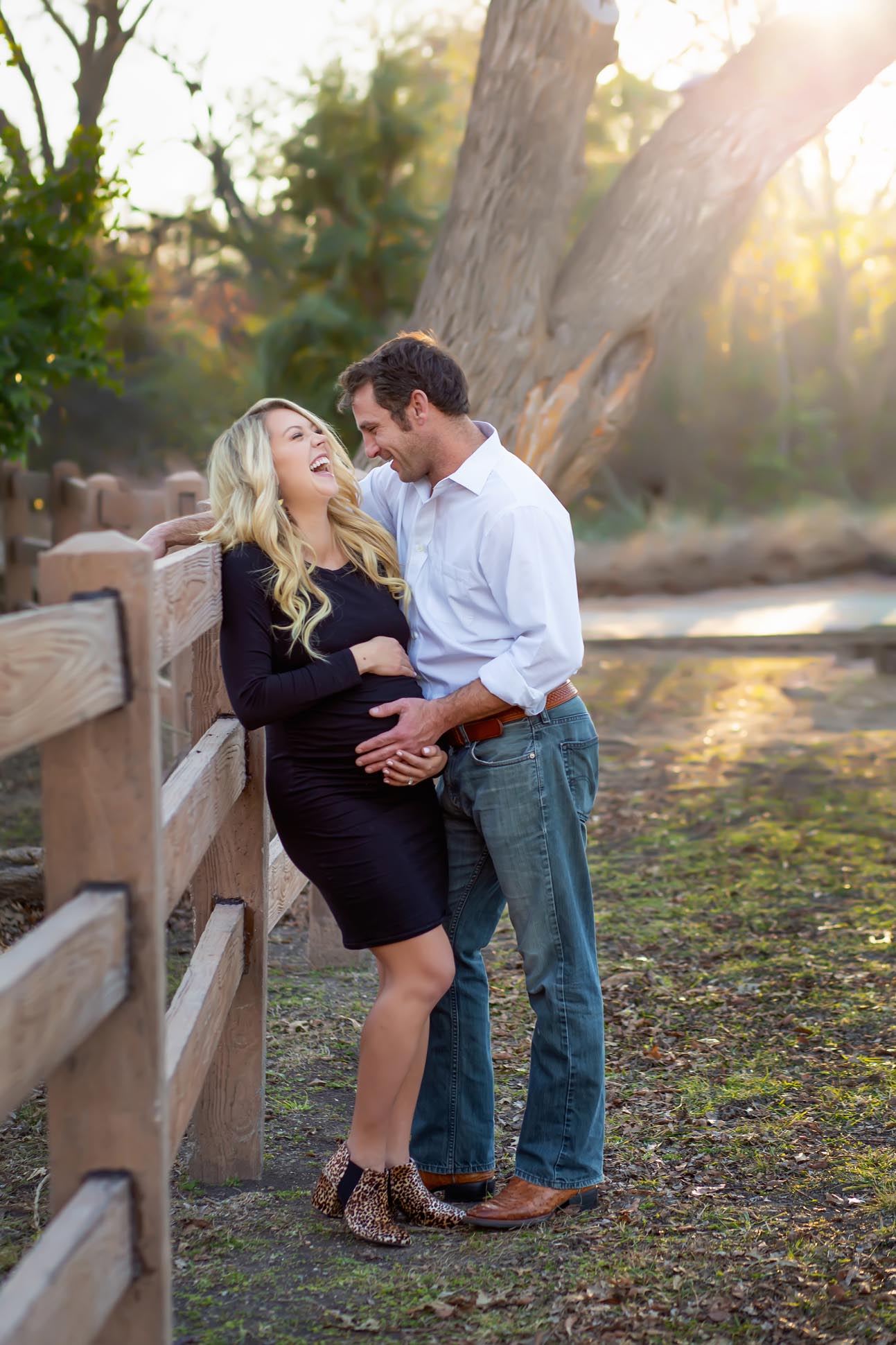 Dallas maternity photographer shares picture of couple expecting baby next to western fence at Prairie Creek Park in Richardson Texas, mom to be is wearing short black dress, dad is in jeans and white button down shirt
