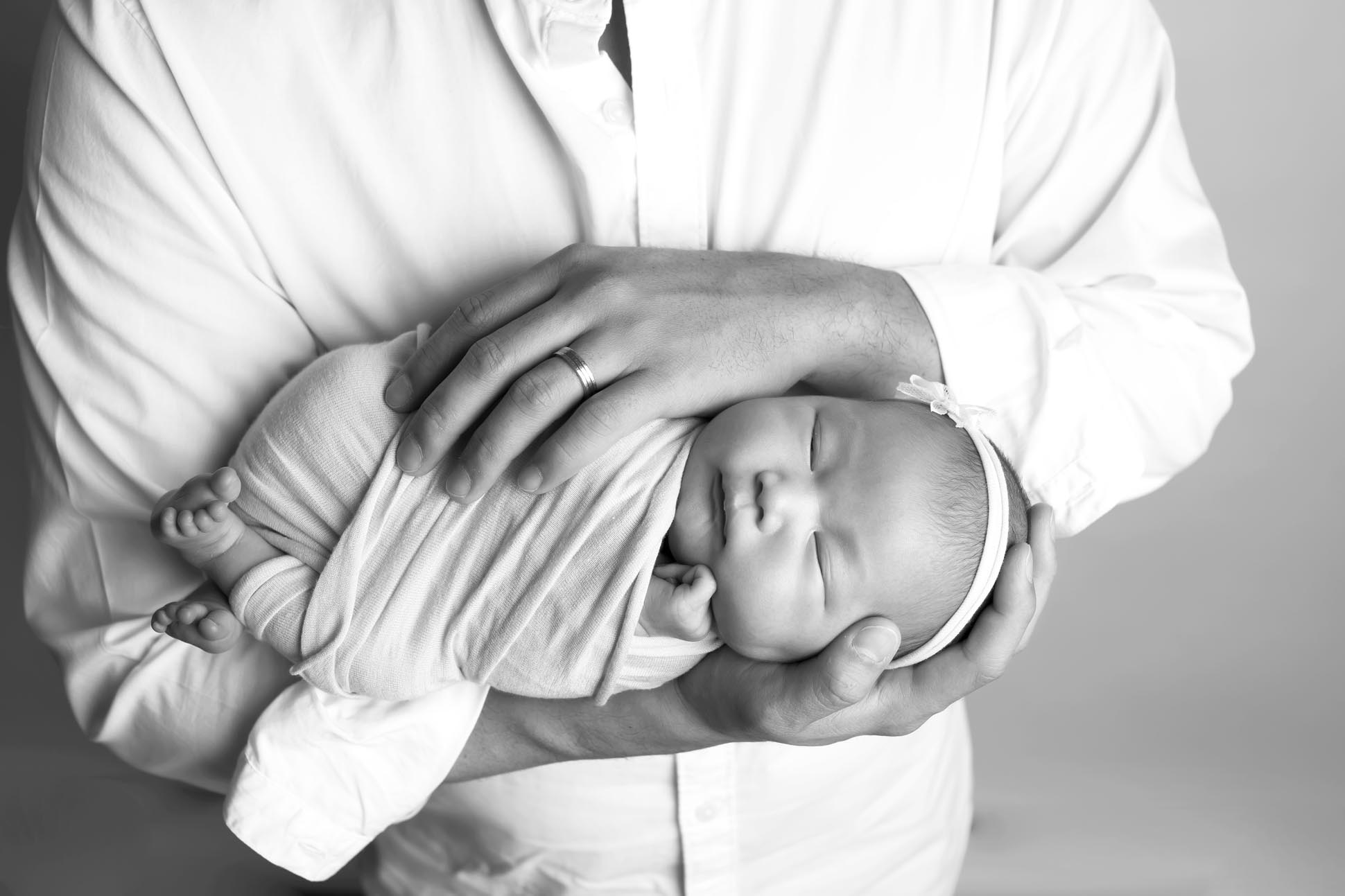 Dallas newborn photographer poses newborn baby in dads arms in a football hold, portrait is finished black and white