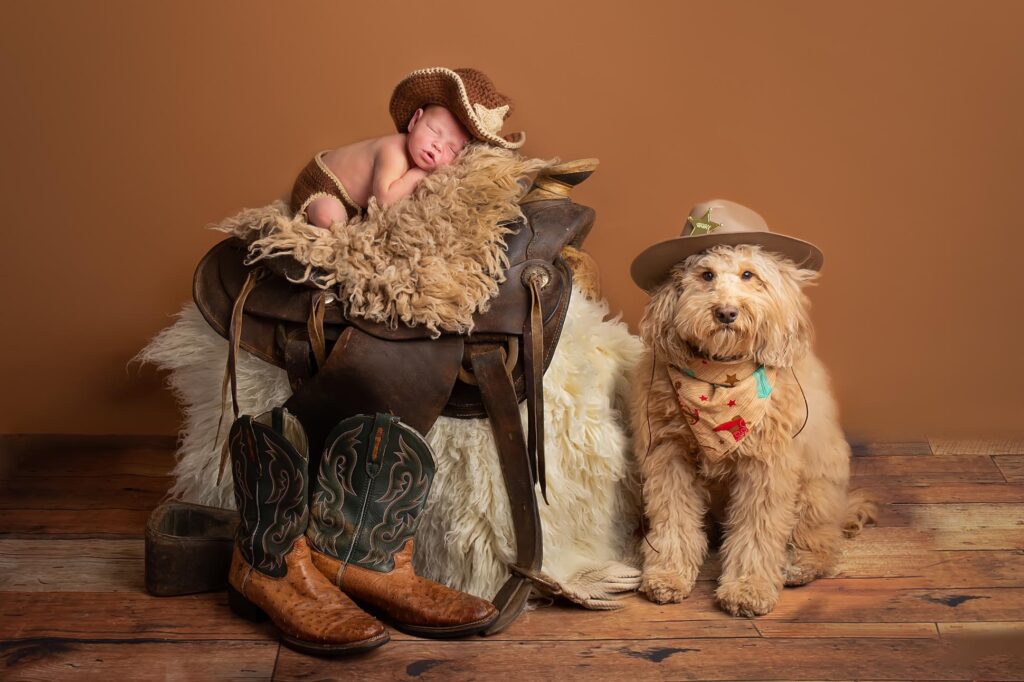 Dallas newborn poses with his best friend goldendoodle ranger baby is posed on western saddle with his dads boots nearby and dog next to him wearing cowboy hat in Dallas texas