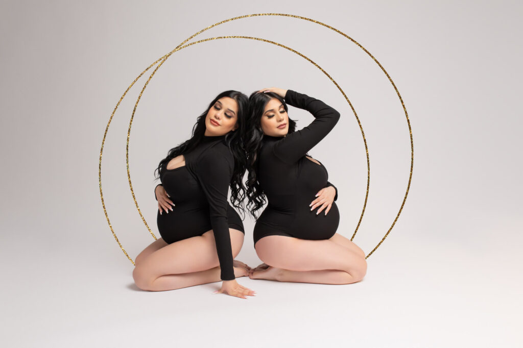 Identical twin sisters expecting two weeks apart pose for their maternity photography session at Dallas maternity photographer Mod L Photography studio back to back wearing black bodysuits