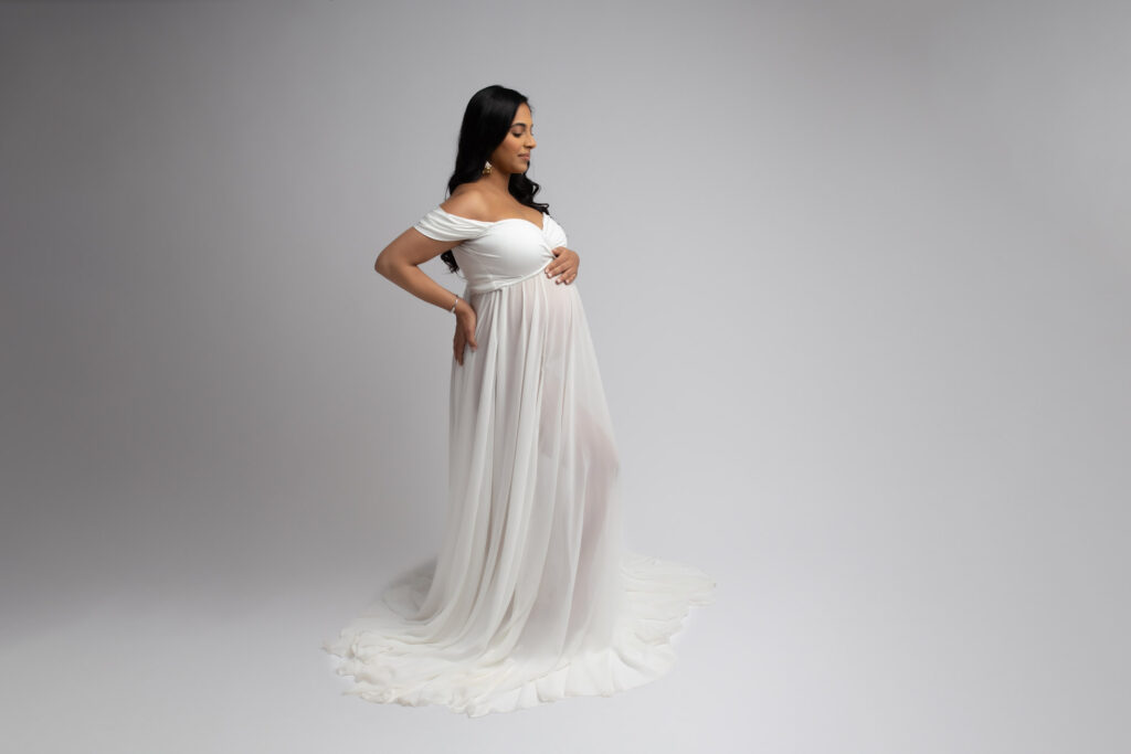Dallas maternity photographer poses client in white organza skirt dress on gray background during her maternity photography session