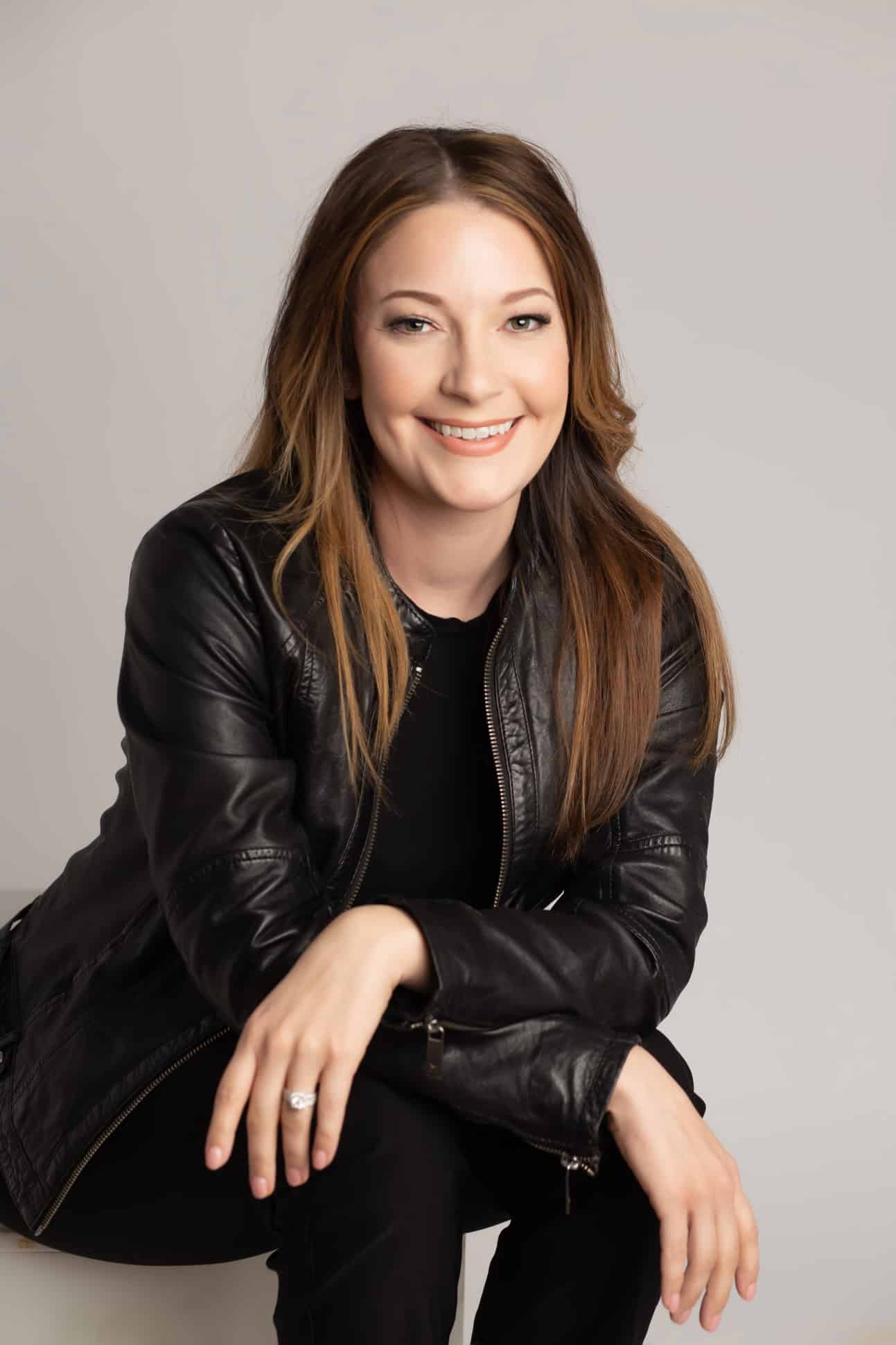 Headshot and branding portrait of brunette wearing black leather jacket on light gray background in a relaxed pose in Dallas Texas