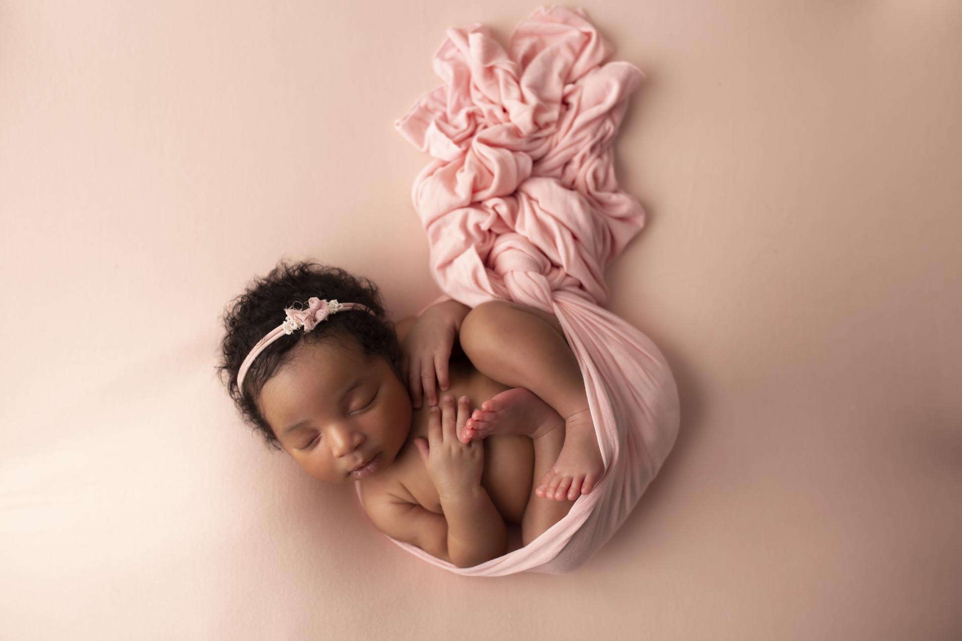 Dallas newborn photographer poses infant baby girl on pink blanket, wrapped in pink blanket with headband during newborn photography session