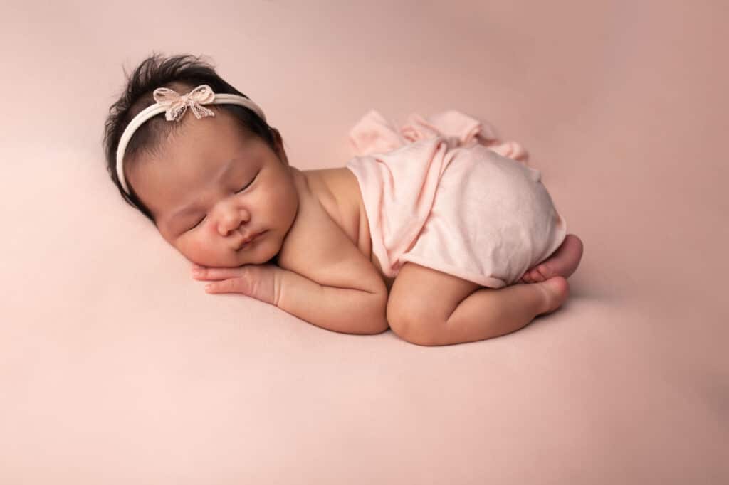 Sweet baby girl wrapped in pink on a pink blanket with a cute pink headband photographed by Dallas newborn photographer Mod L Photography owner Laura Levitan in Addison, TX
