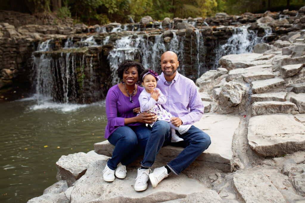 18 month old girl pictured in front of water fall with parents all dressed in coordinating purple outfits by Mod L Photography