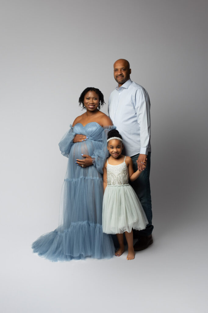 Expectant family pictured in shades of blue big sister, pregnant mom and dad pose in Mod L Photography portrait studio for maternity session in Addison Texas with Laura Levitan