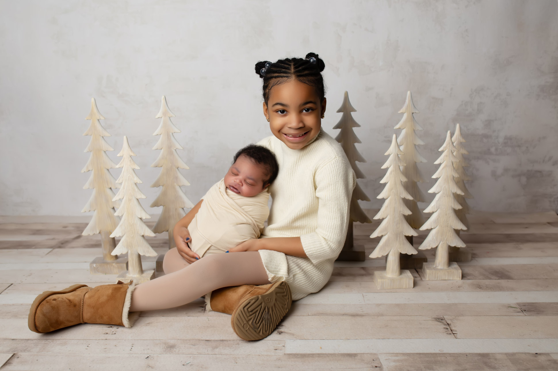 Portrait of big sister holding baby brother in neutral toned Christmas themed photograph in studio by Mod L Photography