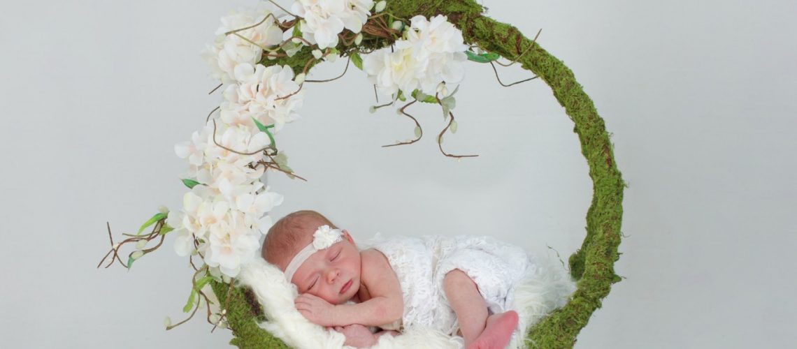 Composite newborn image of baby in floral and moss swing on a white background.