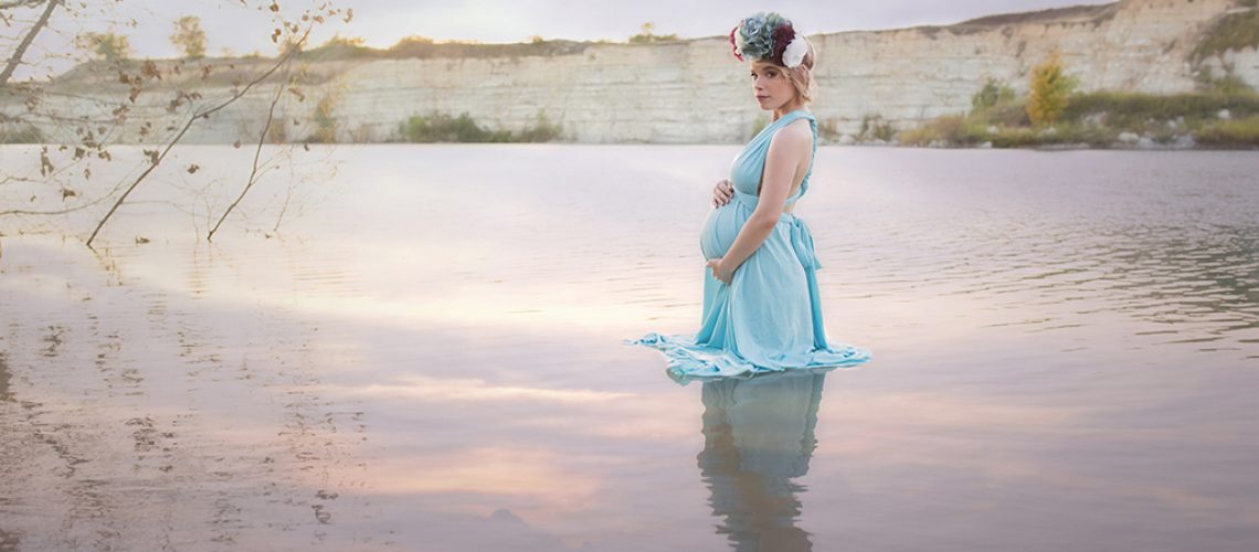 Dallas mom to be wading in the lake at sunset wearing a blue dress and floral corwn